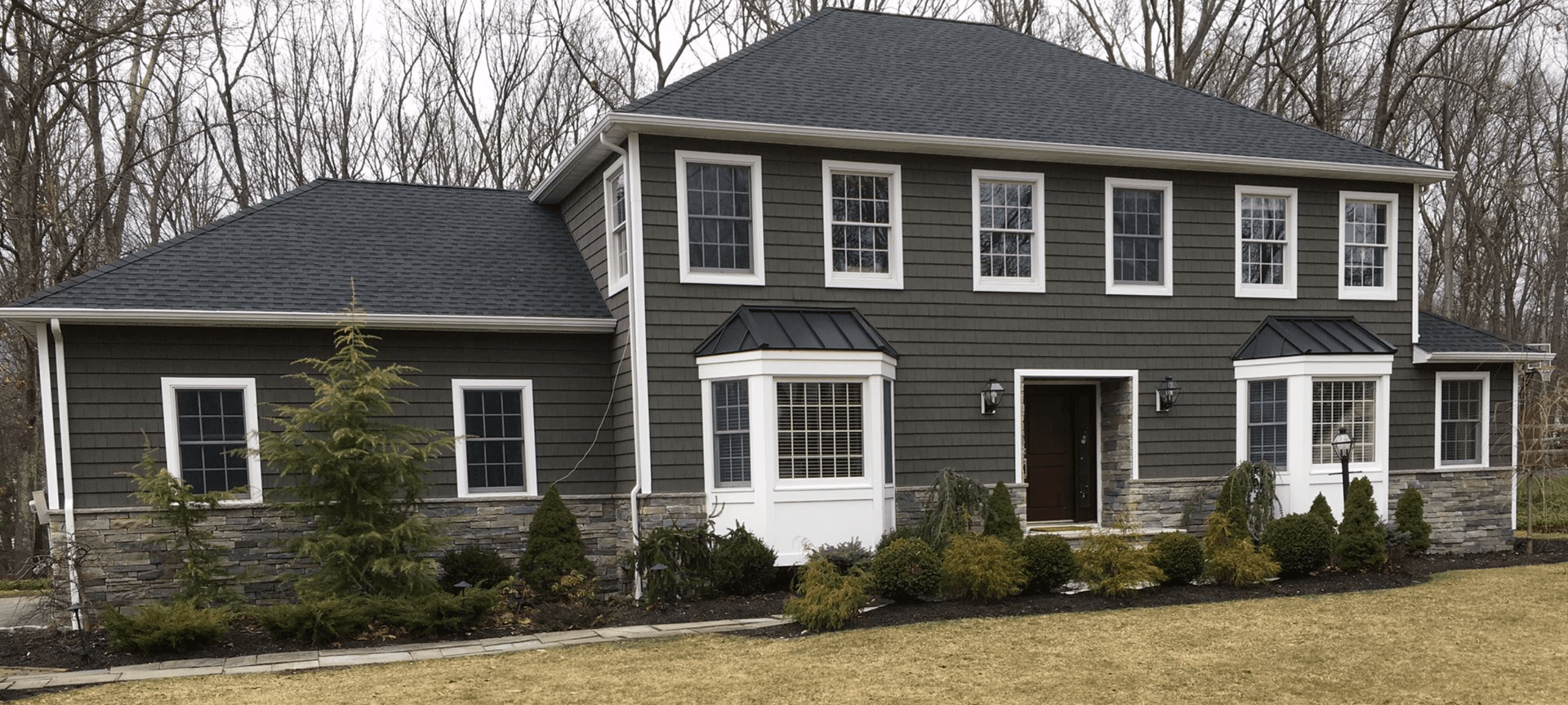 Two-story dark gray house with white trim, multiple windows, and a shingled roof, viewed from the front.