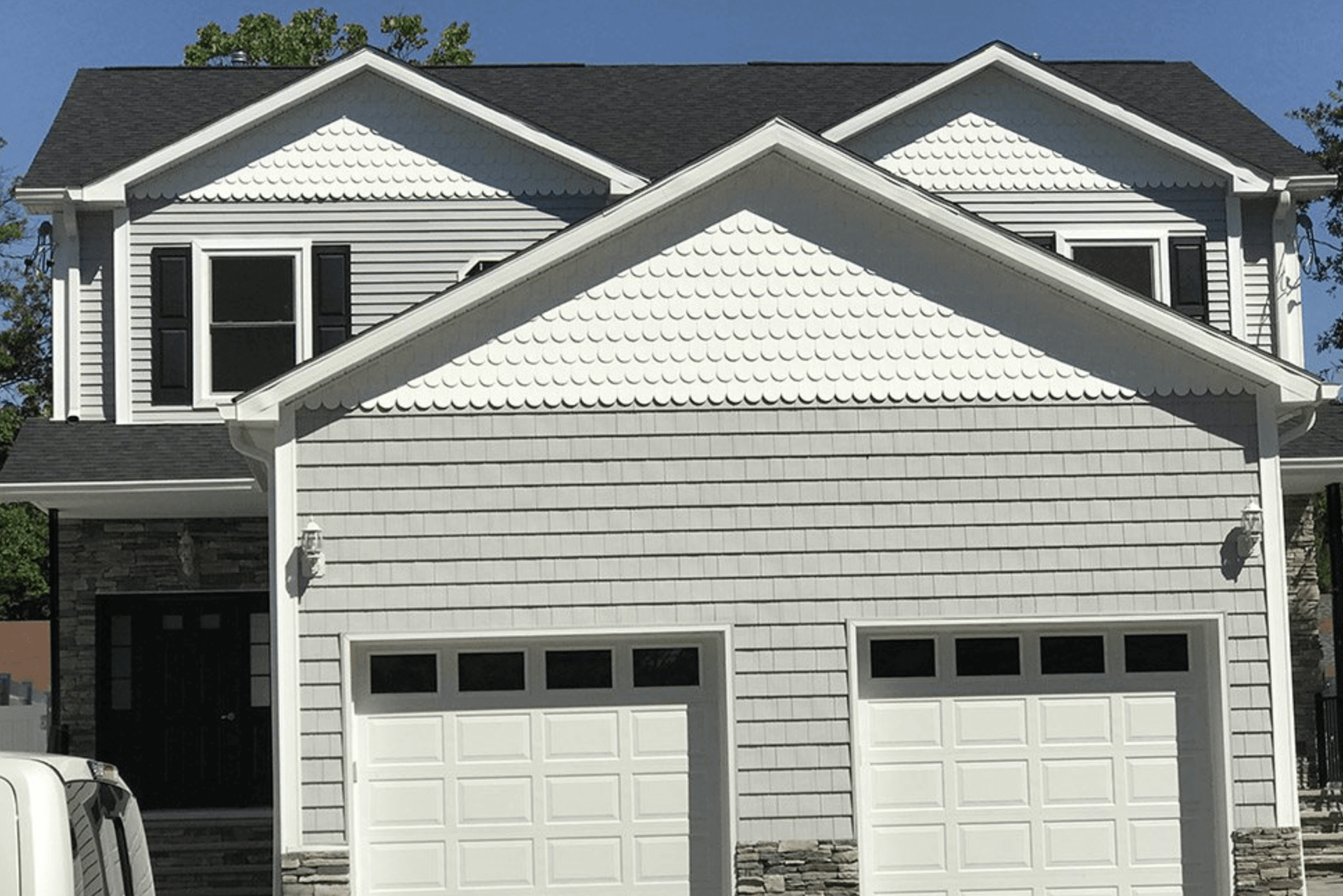 Two-story suburban house with white siding and a double garage under a blue sky