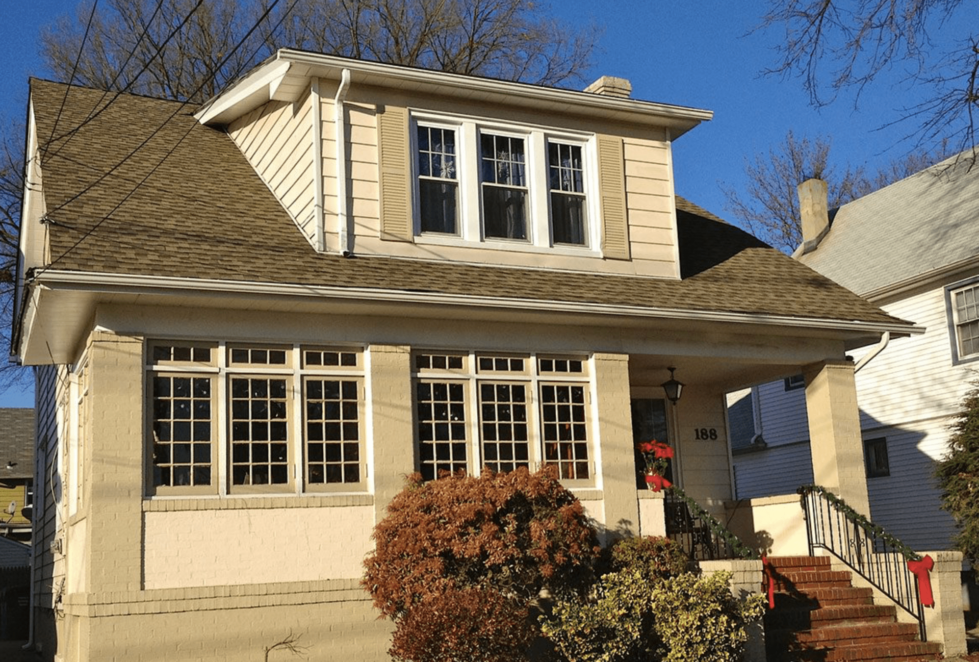 Two-story beige house with a front porch, dormer windows, and steps leading up from the yard