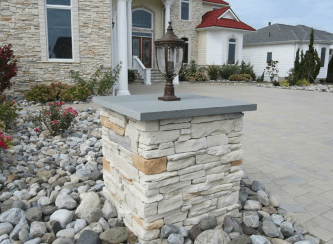 Stone pillar light fixture in a landscaped driveway beside a house.