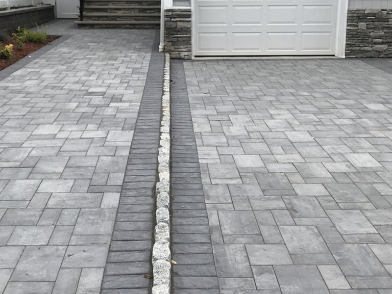 Gray paved driveway with a central drainage strip leading to a garage door and front steps