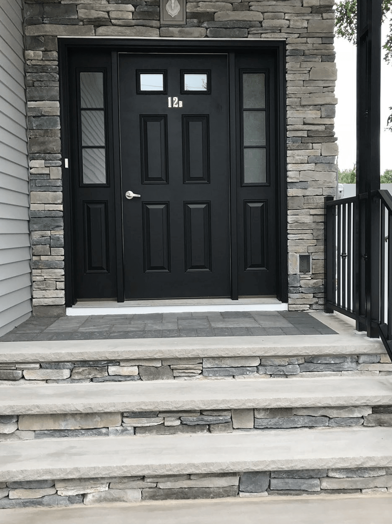 Black front door with small windows, framed by stone siding and steps leading up to the entrance.