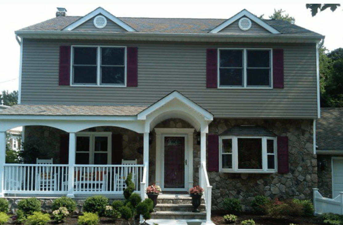 Two-story house with gray siding, brick accents, white porch, and red shutters