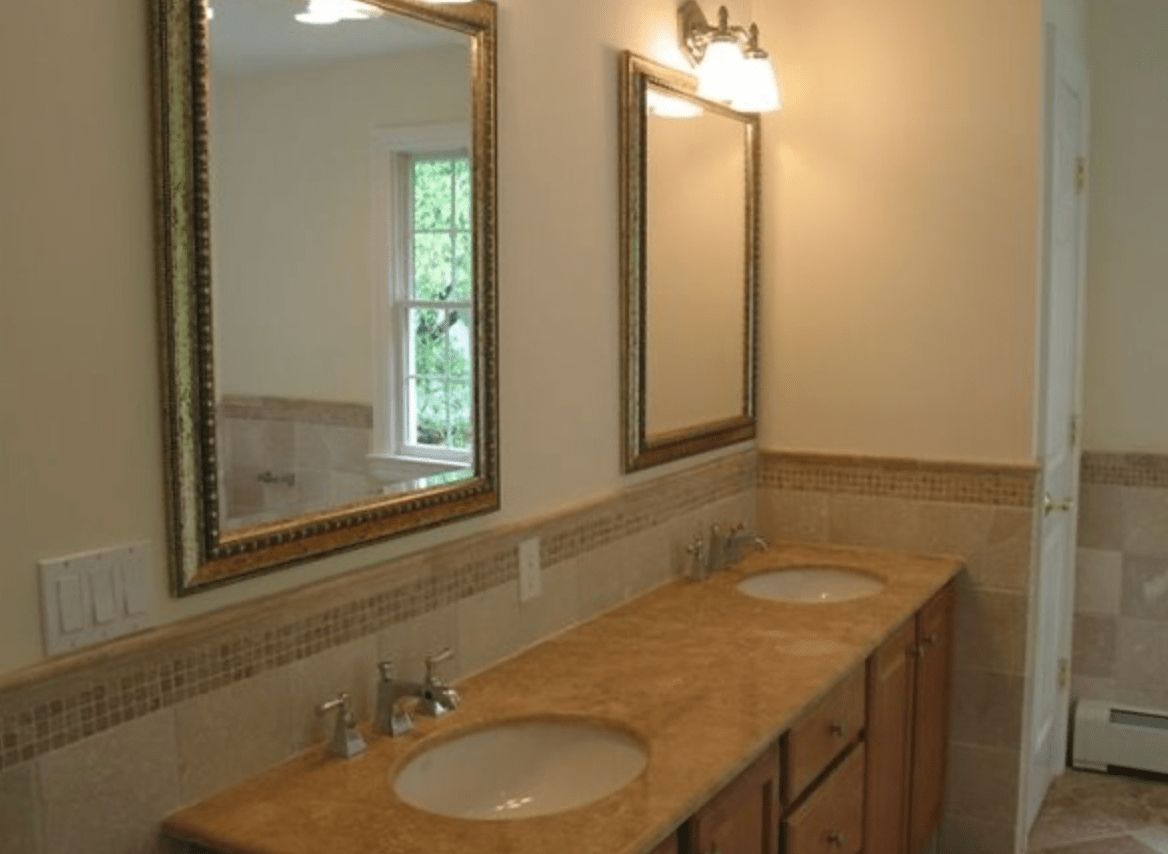 Bathroom vanity with two sinks, large mirrors, and beige tile walls
