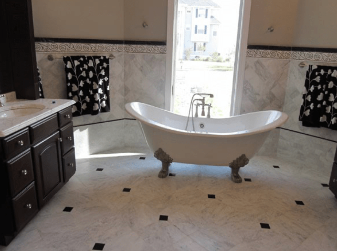 Elegant bathroom with a freestanding white bathtub, dark cabinets, and a bright window.