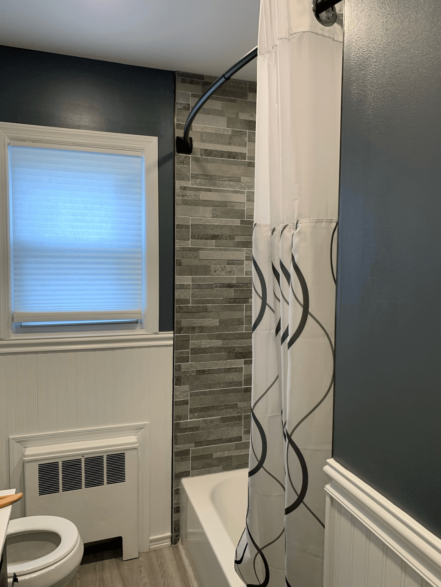 Small bathroom with toilet, window, shower curtain, and gray tiled shower wall