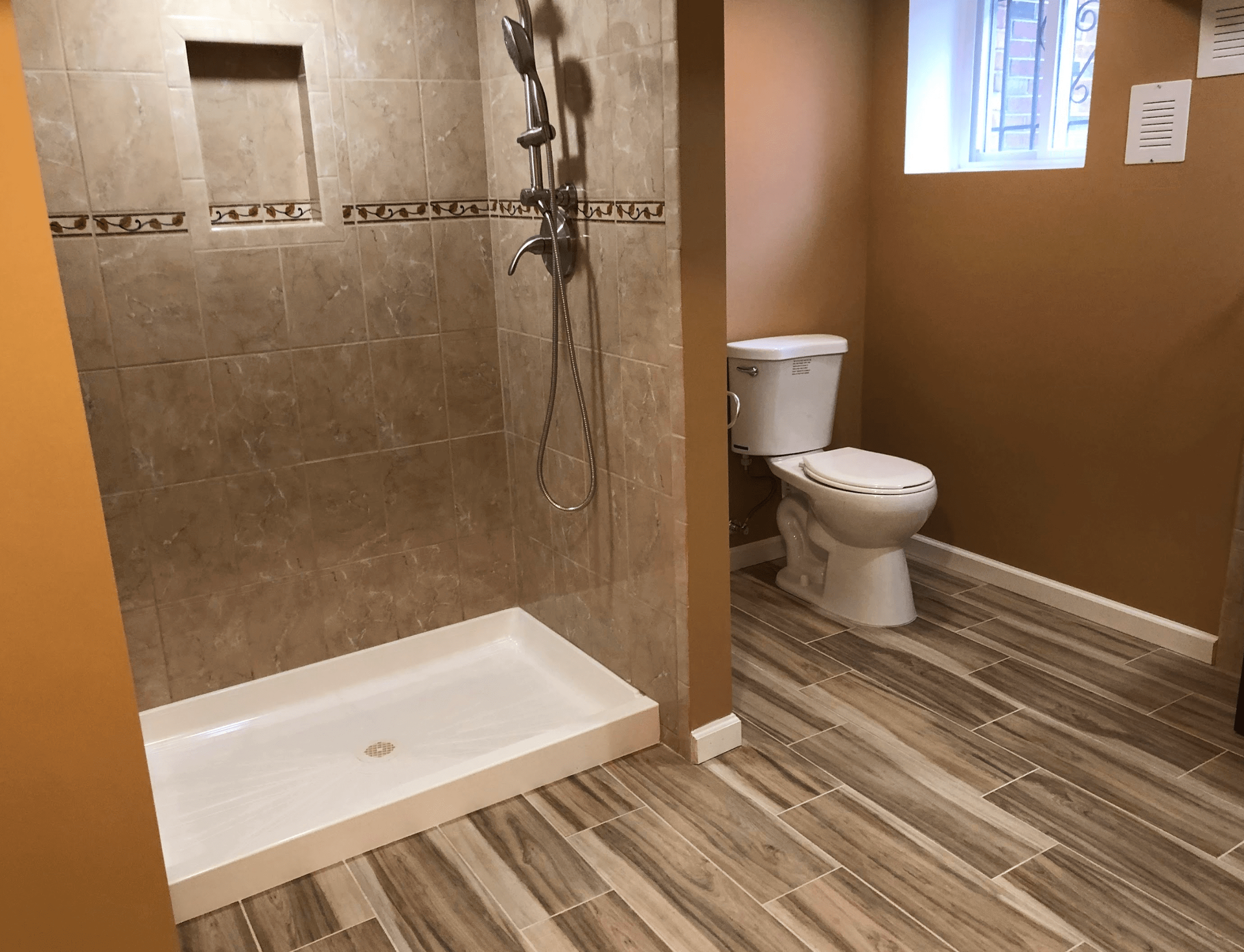 Accessible bathroom with walk-in shower, toilet, and brown tile walls and wood-look floor.