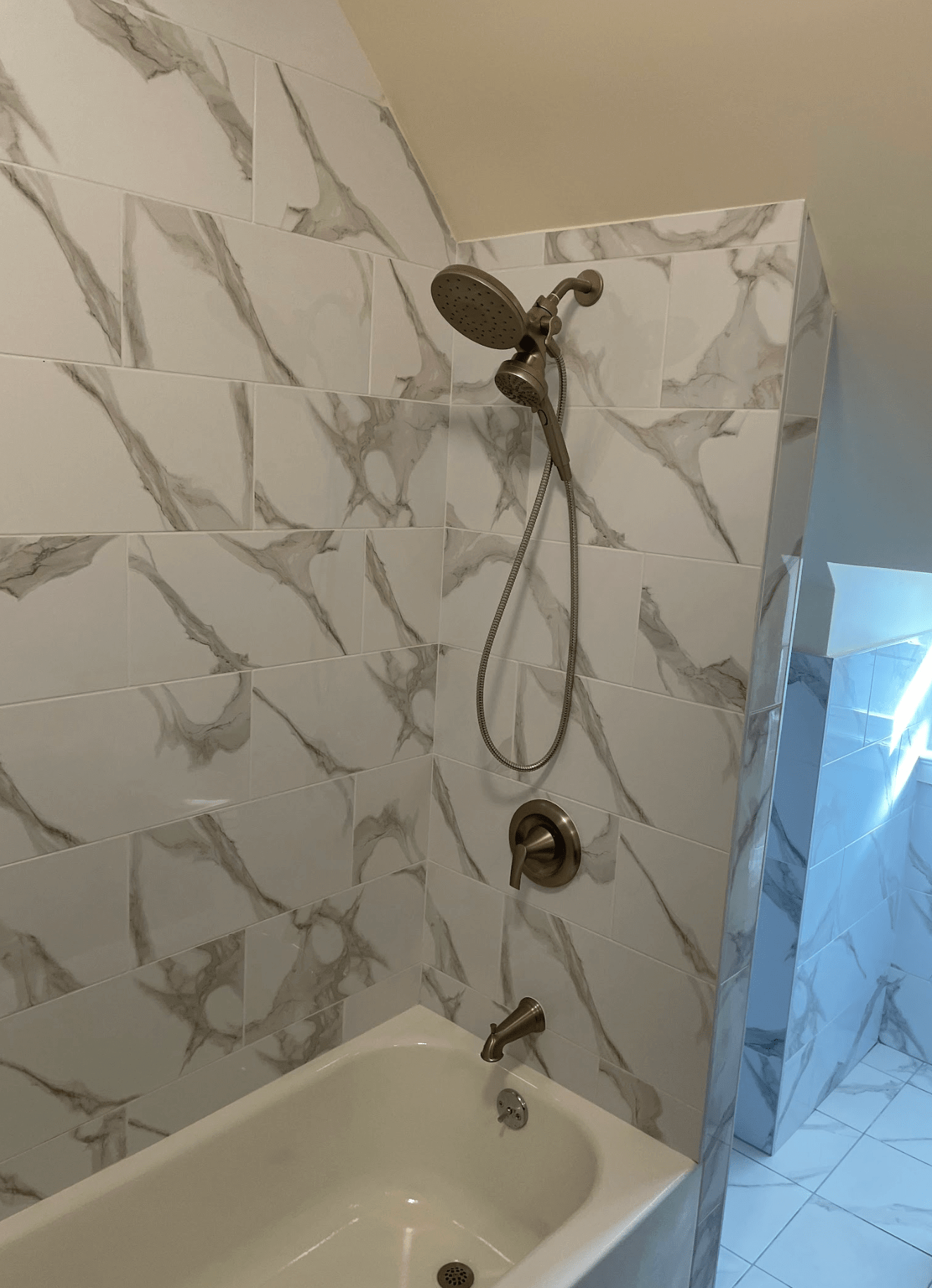 Bathtub shower with marble-pattern tile wall and handheld showerhead in a bathroom