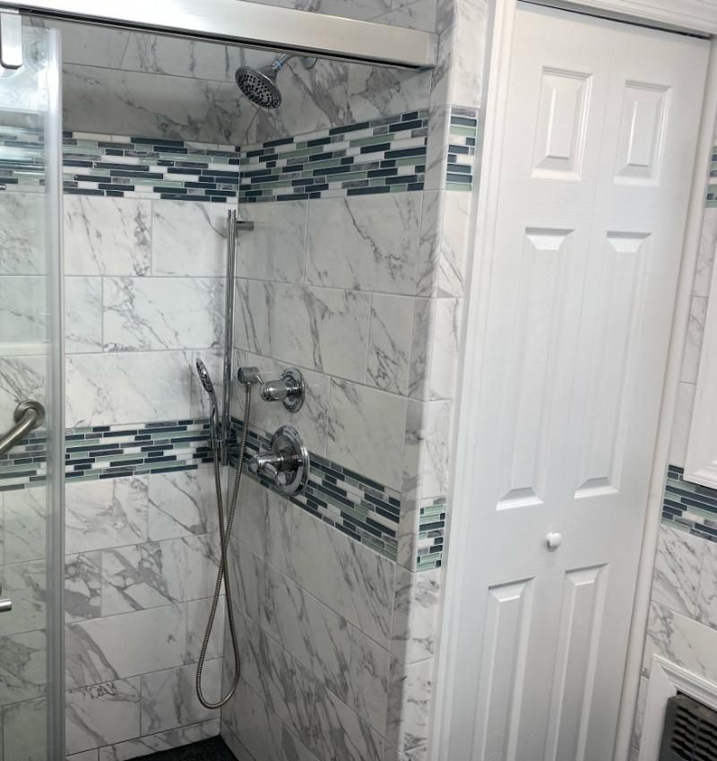 Tile shower with glass door and silver fixtures beside a white paneled door.
