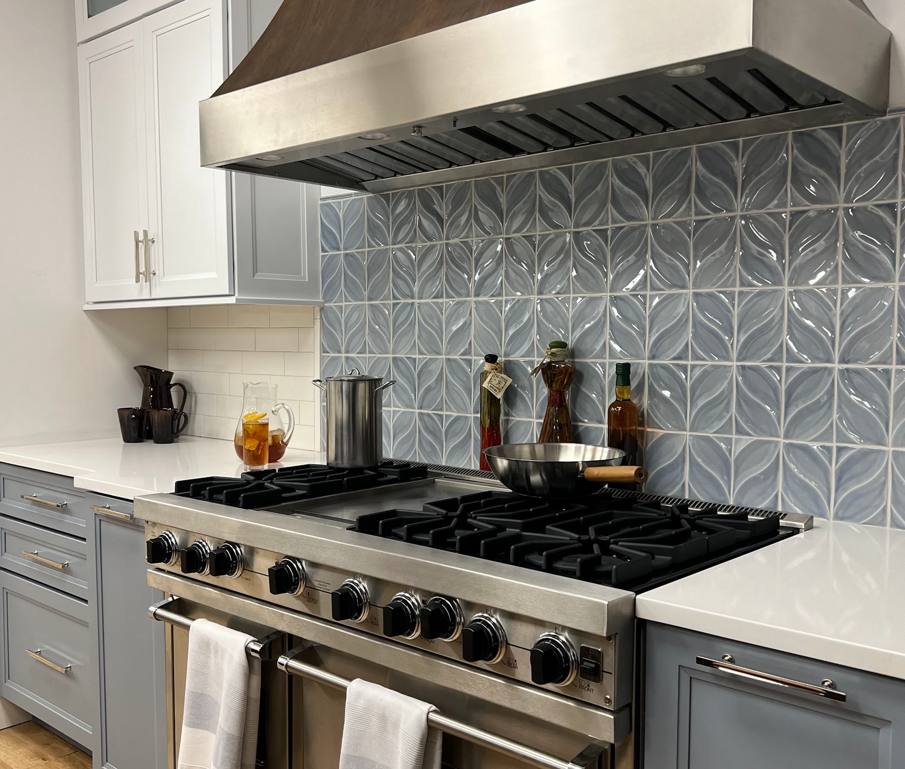 Modern kitchen with stainless steel stove, white cabinets, and blue patterned backsplash under a vent hood
