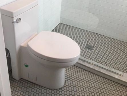 White toilet in a tiled bathroom with a curbless shower and floor drain