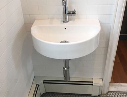 White wall-mounted bathroom sink with chrome faucet above a floor drain