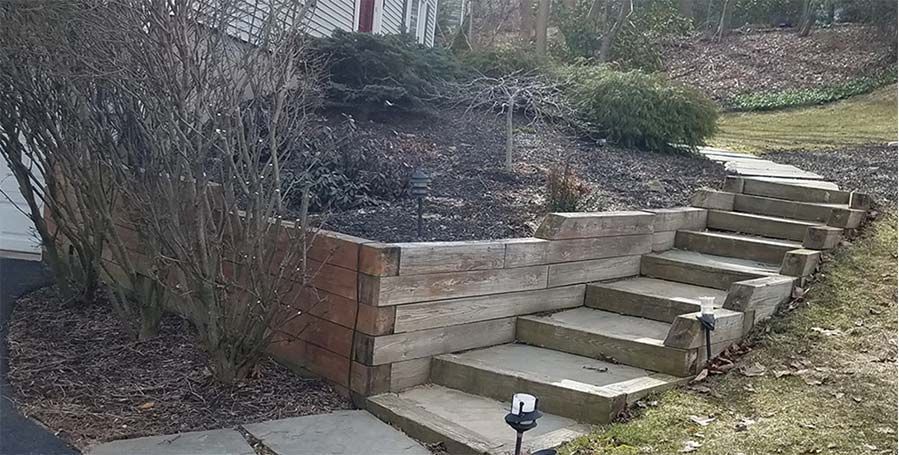 Stepped stone retaining wall with stairs beside a leafless shrub in a yard