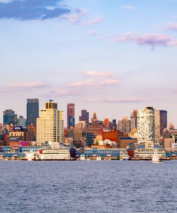 City skyline across a harbor at dusk, with colorful buildings under a pink-blue sky.