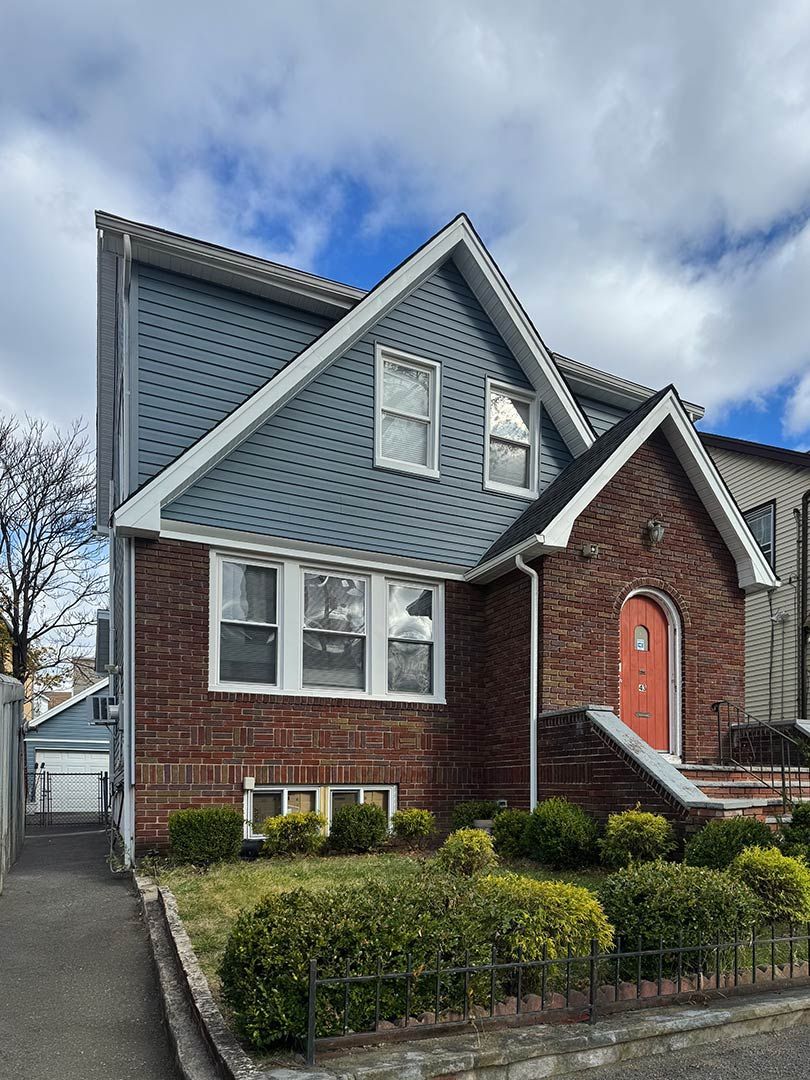 Brick house with blue shingled roof, front steps, and trimmed hedges on a cloudy day
