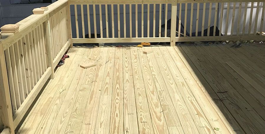 Sunlit wooden deck with white railings and stairs, viewed from above.
