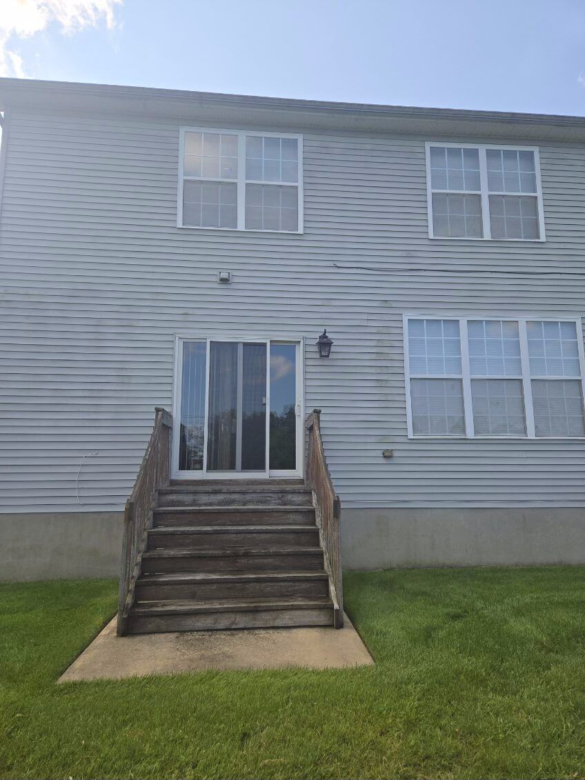 Exterior of a beige townhouse with front stairs, white windows, and a small lawn