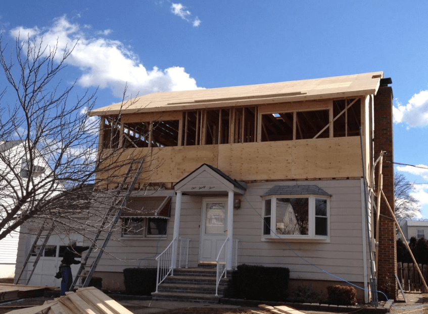 Partially demolished two-story house with exposed framing under a blue sky