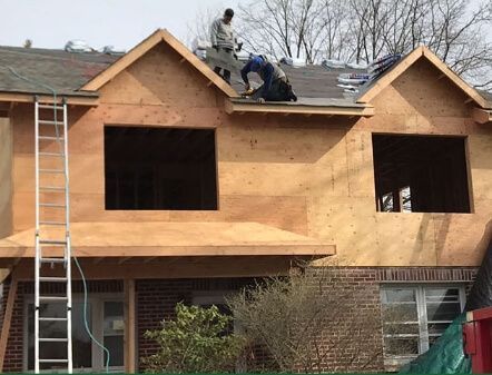 Workers roofing a two-story house with plywood siding and two gable dormers