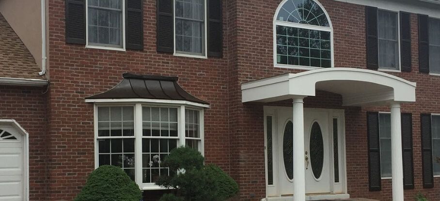 Brick townhouse facade with white trim, arched front porch, bay window, and shrubs