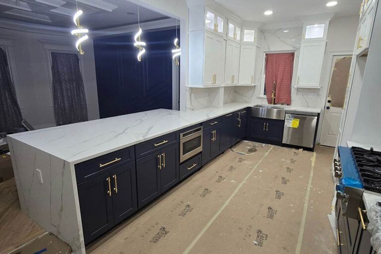 Modern kitchen with dark cabinets, white counters, pendant lights, and cardboard covering the floor during renovation