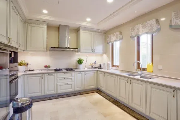 Bright white kitchen with cream cabinets, marble countertops, and two windows with valances