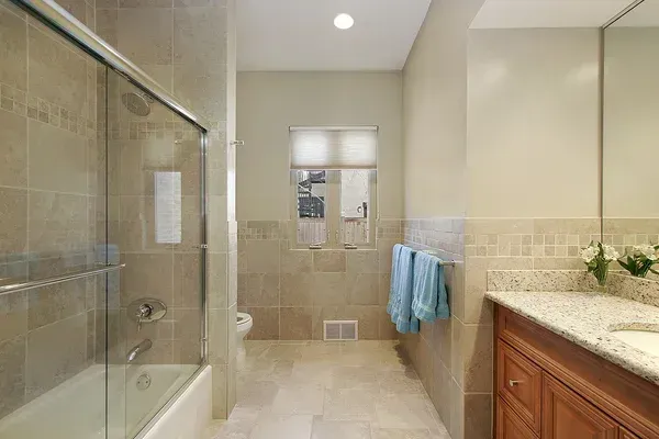 Modern beige bathroom with glass shower, tub, vanity, and blue towels