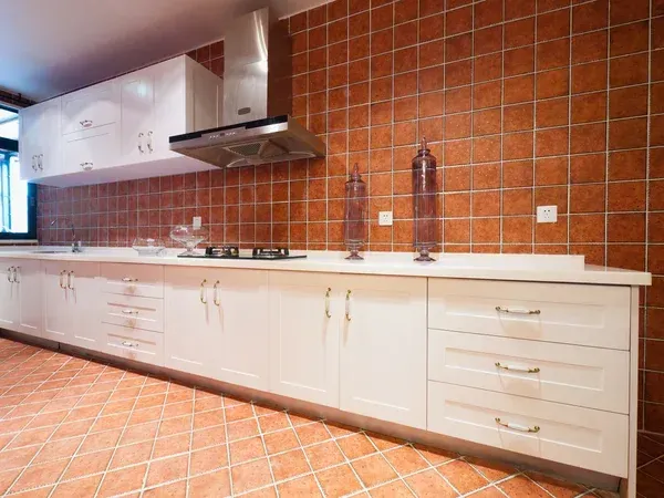 Modern kitchen with orange tile floor and backsplash, white cabinets, and stainless steel range hood