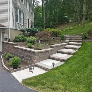 Stone steps and retaining wall beside a house, leading up a landscaped grassy hillside.