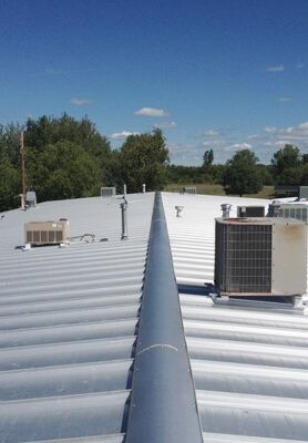 Rooftop with white metal panels, HVAC units, and a clear blue sky above trees.