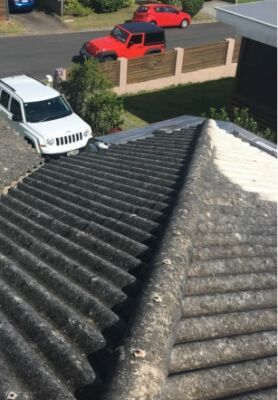 View from a corrugated roof toward a driveway with two red vehicles and a white SUV near a brick wall.