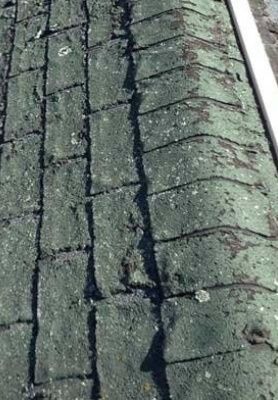 Close-up of a green, weathered shingle roof with a vertical crack and missing pieces