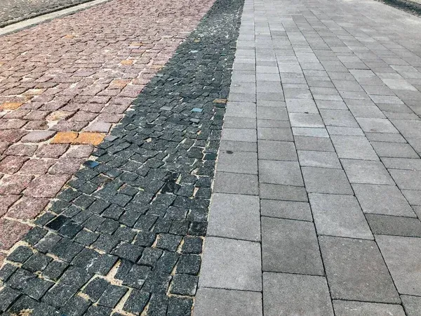 Paved walkway with three textured stone sections in pink, dark gray, and light gray.