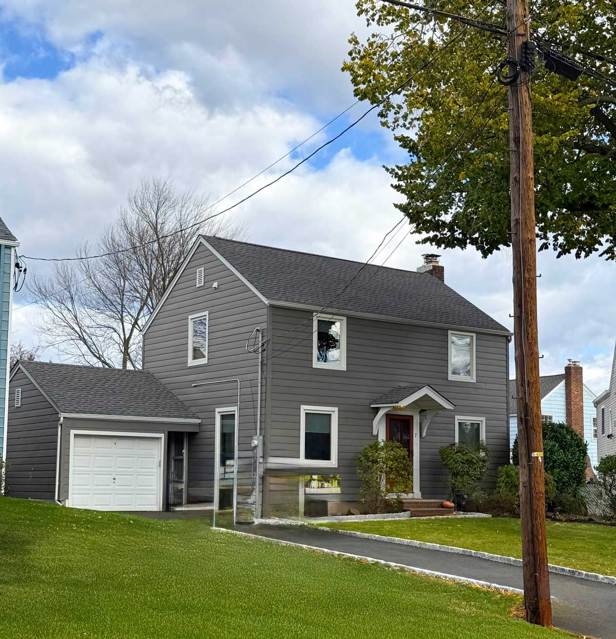 Gray two-story house with attached garage, white trim, and a front lawn on a cloudy day