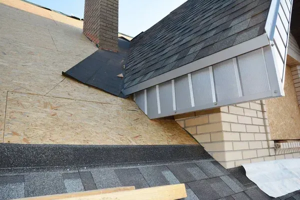 Close-up of a roof junction with shingles, flashing, and brick chimney on a house exterior