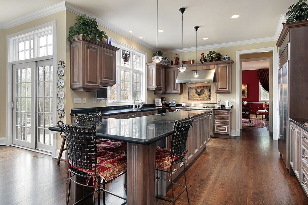 Bright kitchen with dark wood cabinets, granite island, hardwood floors, and a dining area by tall windows