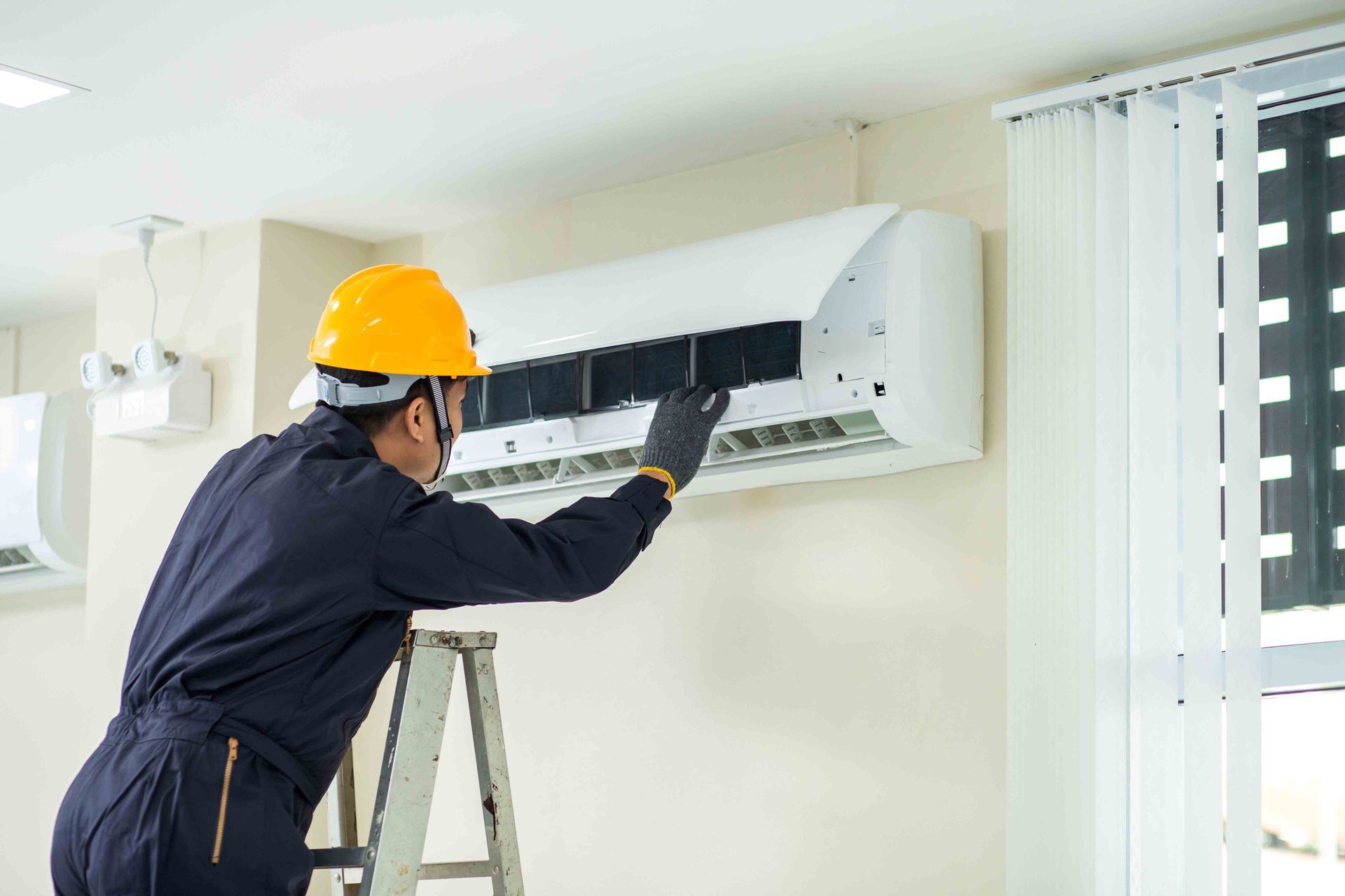 A person on a ladder fixing a air conditioner from a HVAC Installation Contractor