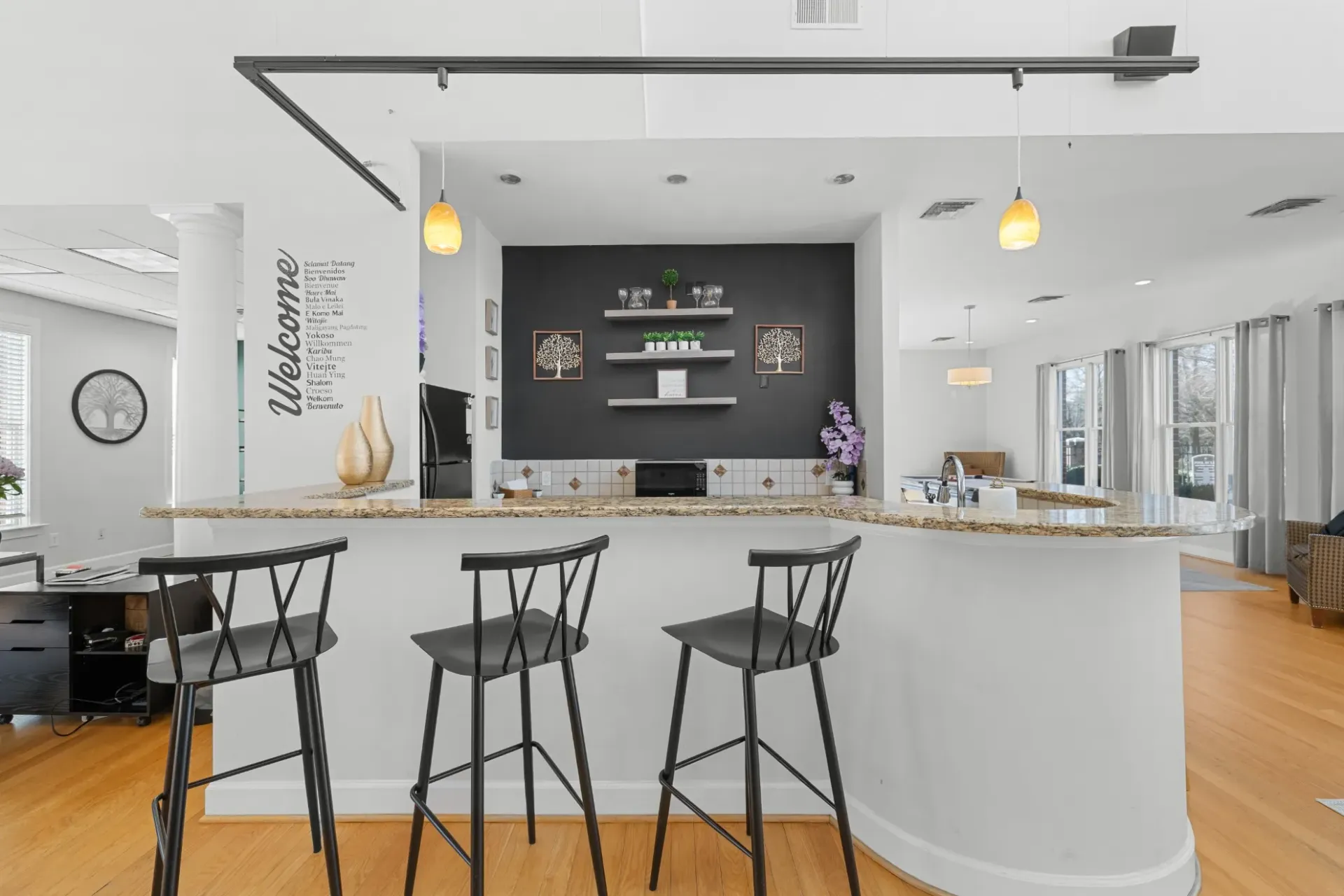 Bright modern kitchen with white island, black stools, pendant lights, and dark backsplash.