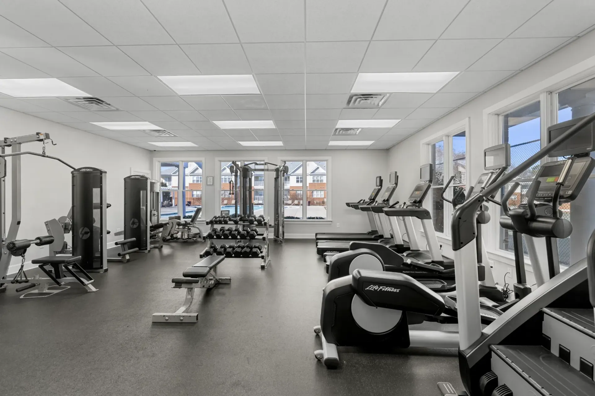 Bright gym interior with cardio machines, weight benches, and large windows