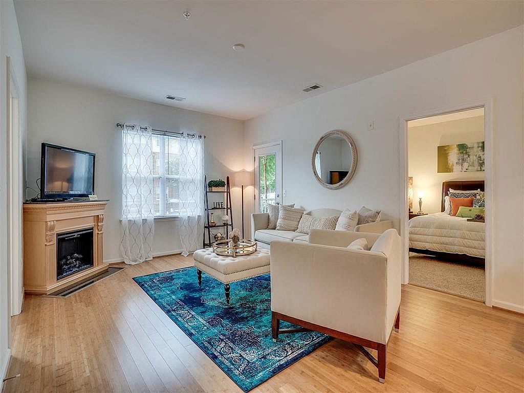 Bright living room with blue rug, beige sofa, TV by fireplace, and open bedroom doorway