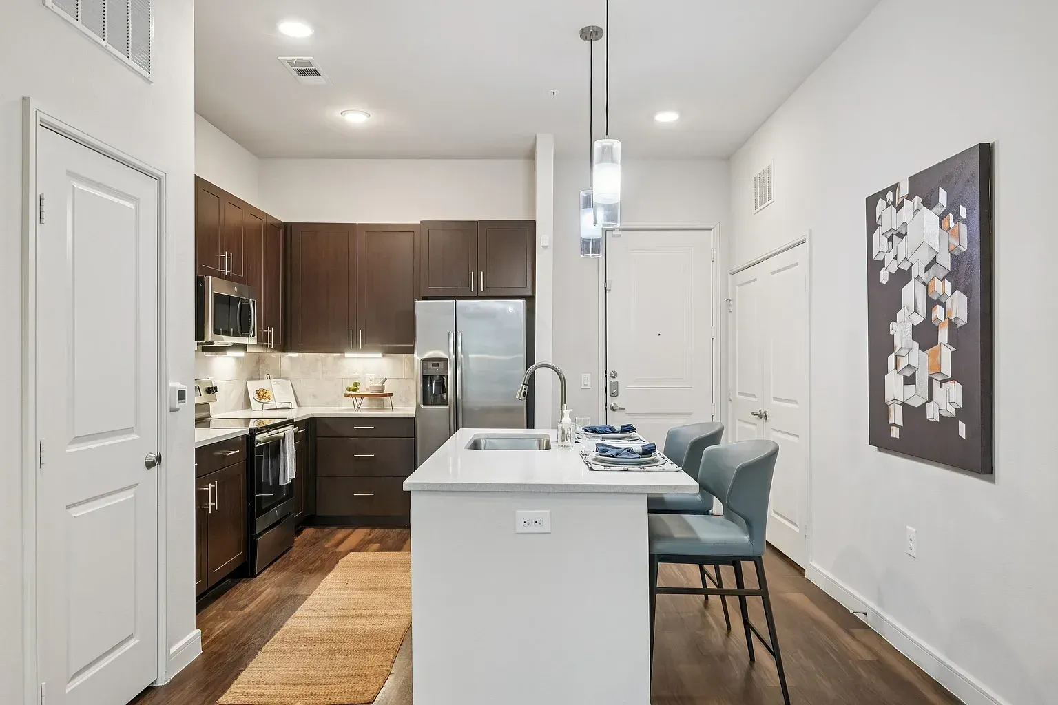 Modern kitchen with dark wood cabinets, stainless steel appliances, and a white island with seating.