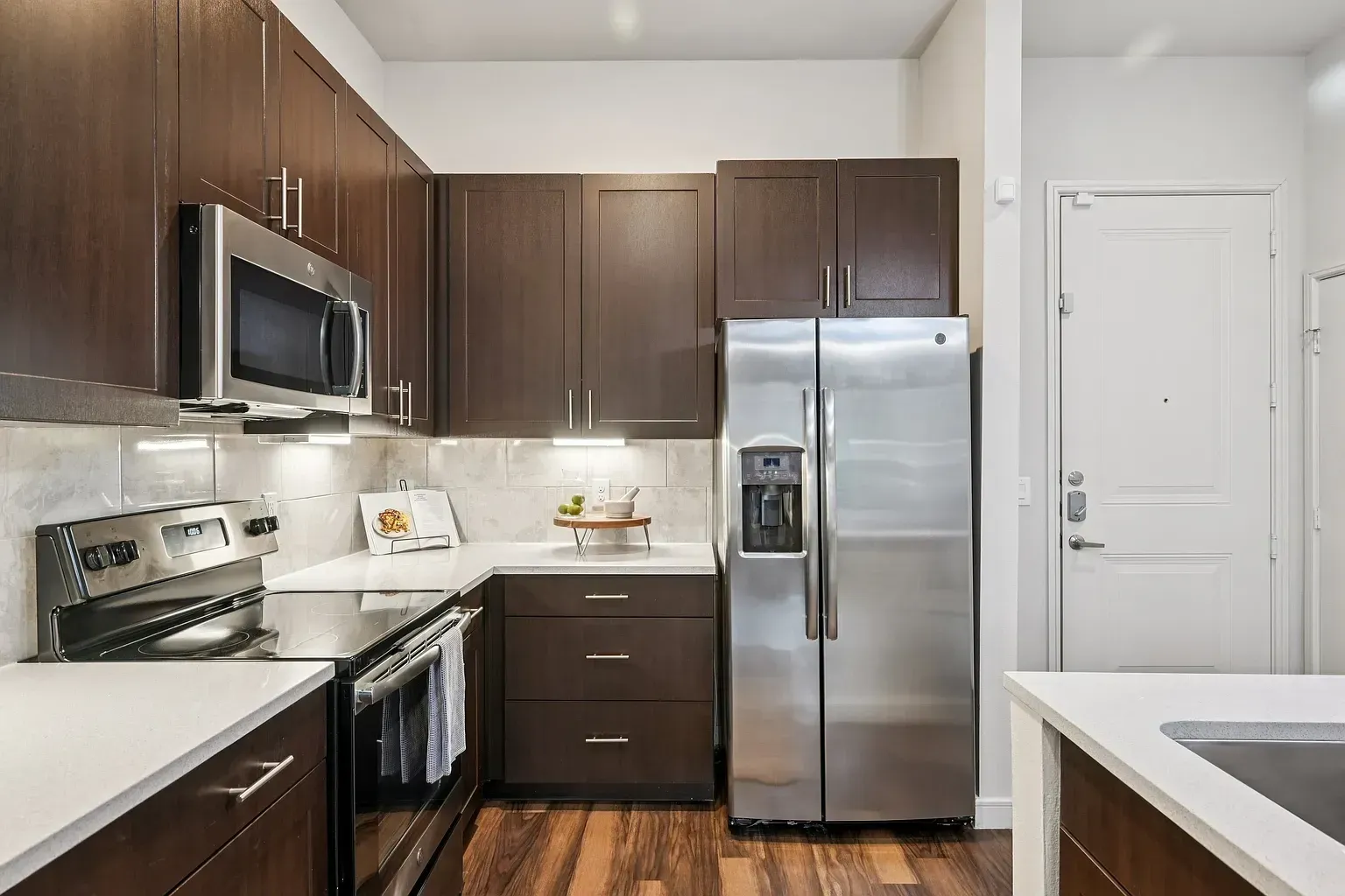 Modern kitchen with dark wood cabinets, stainless steel appliances, and white countertops.
