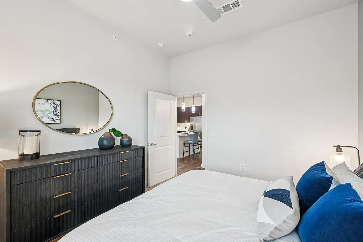 Bedroom with a dresser and a bed, view into the kitchen.
