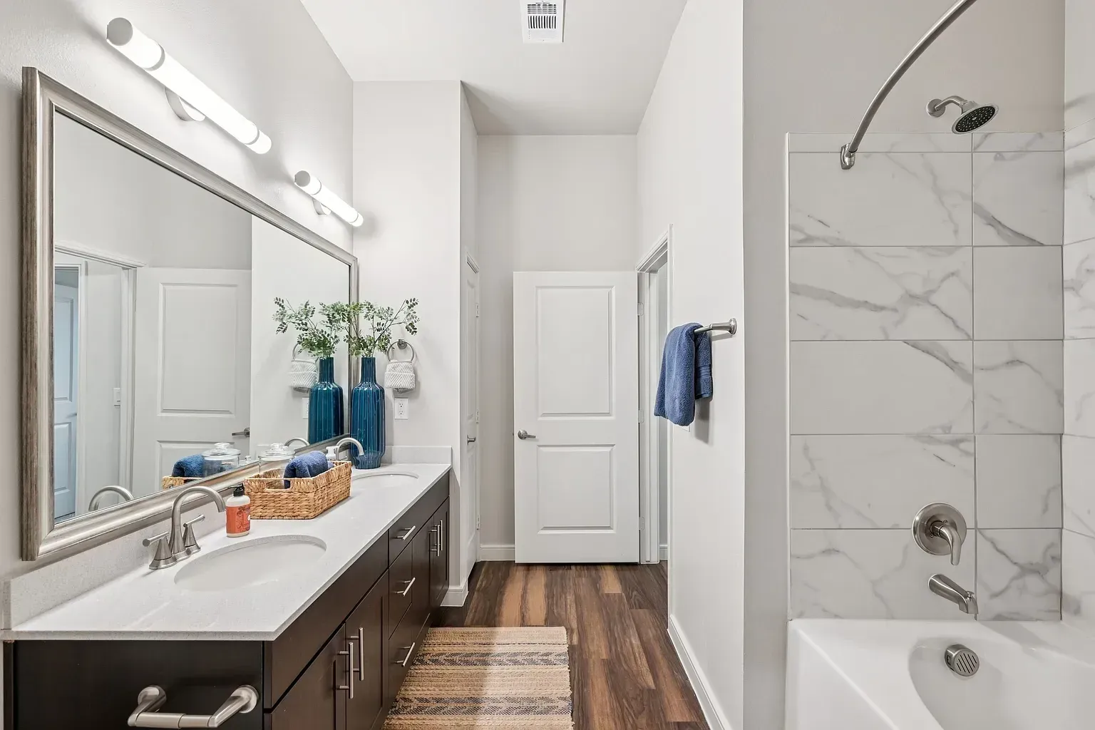 Modern bathroom with double vanity, large mirror, and marble-tiled shower.