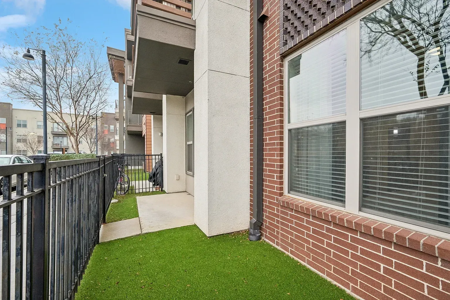 Exterior view of a patio with artificial turf and a black metal fence.