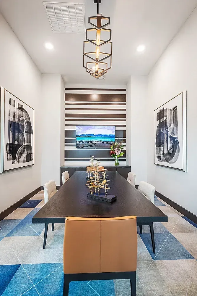 Modern conference room with a long dark wood table, leather chairs, abstract art, and a large TV.