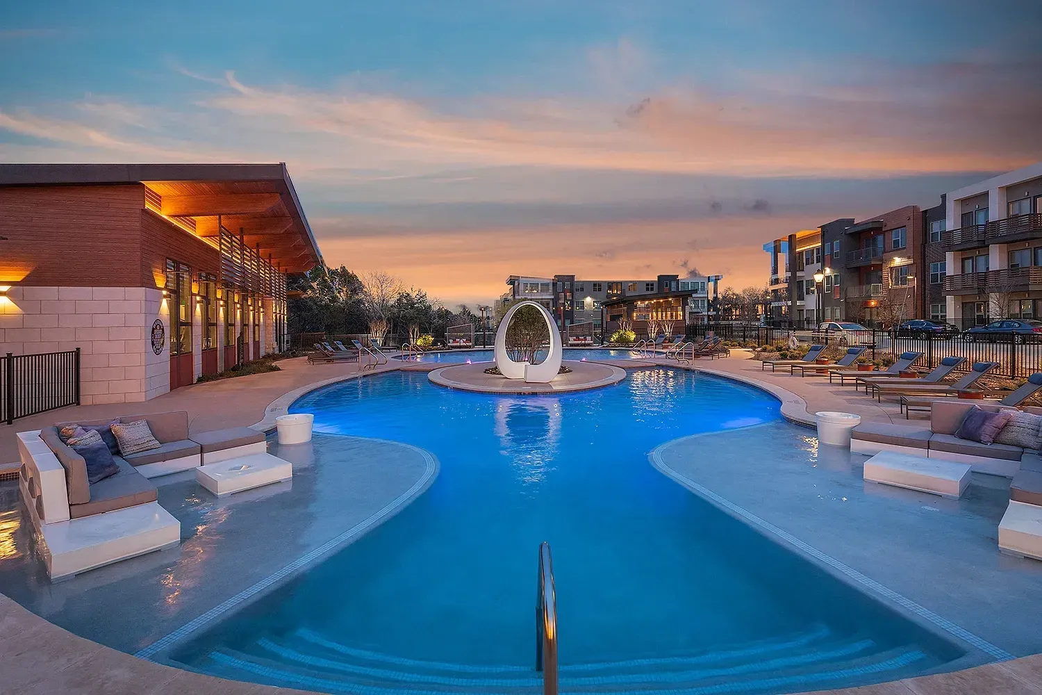 Modern swimming pool with blue lights and lounge chairs at sunset.