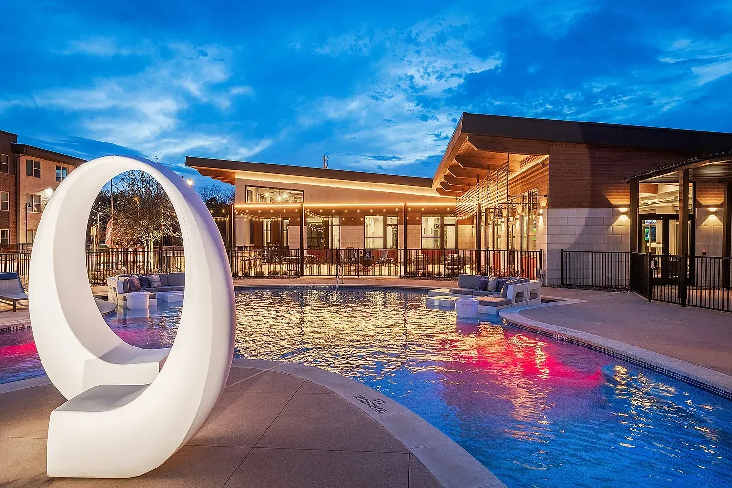 Outdoor swimming pool and lounge area with modern sculpture at dusk.