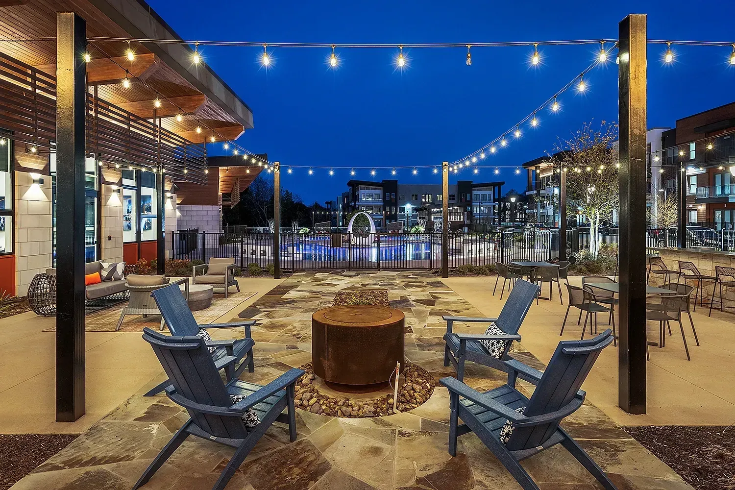 Outdoor patio with fire pit and lounge chairs, overlooking a pool at dusk.