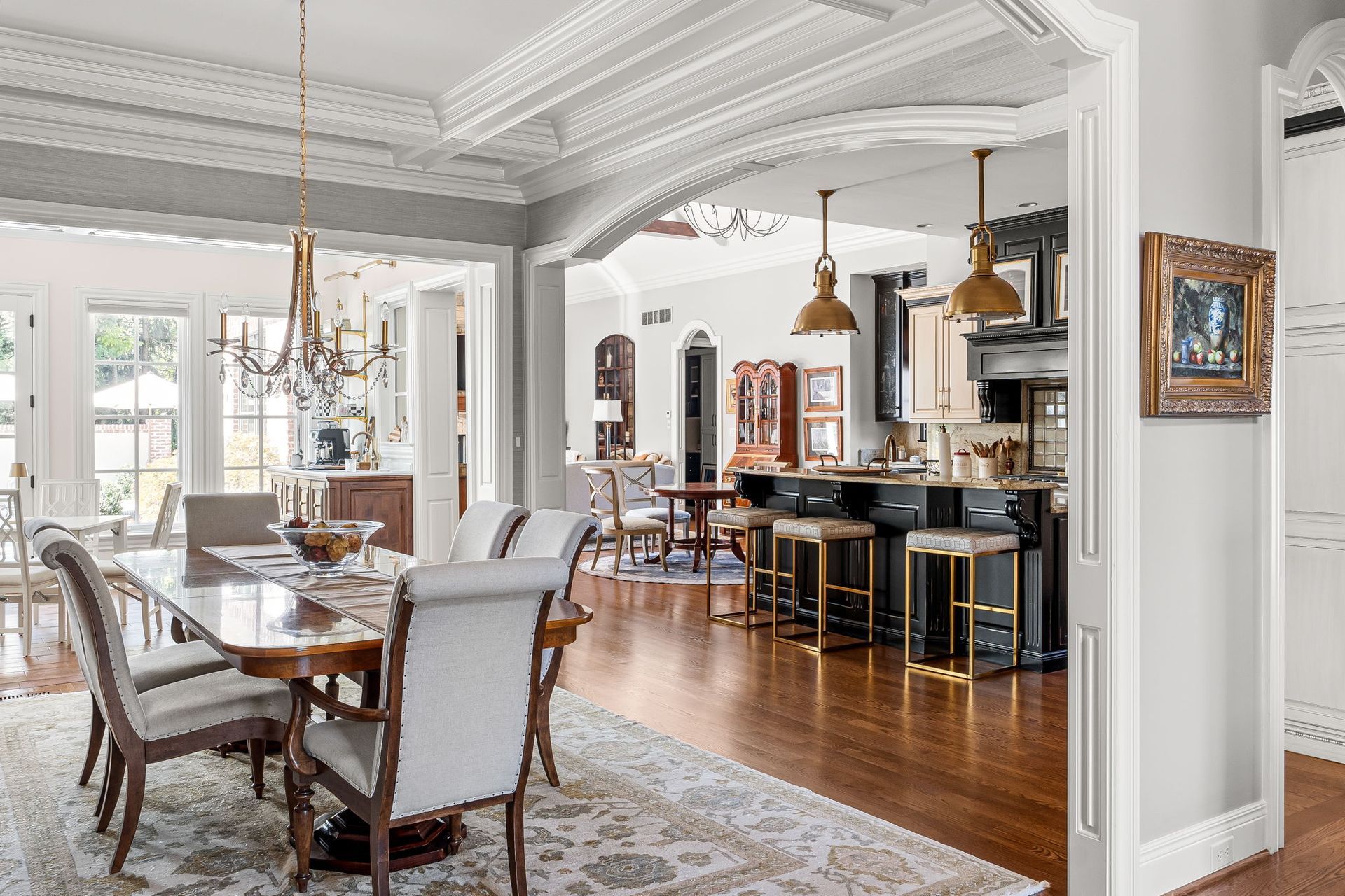 A bright, open-plan dining and kitchen area featuring a dining table with chairs, wood floors, and a dark kitchen island.